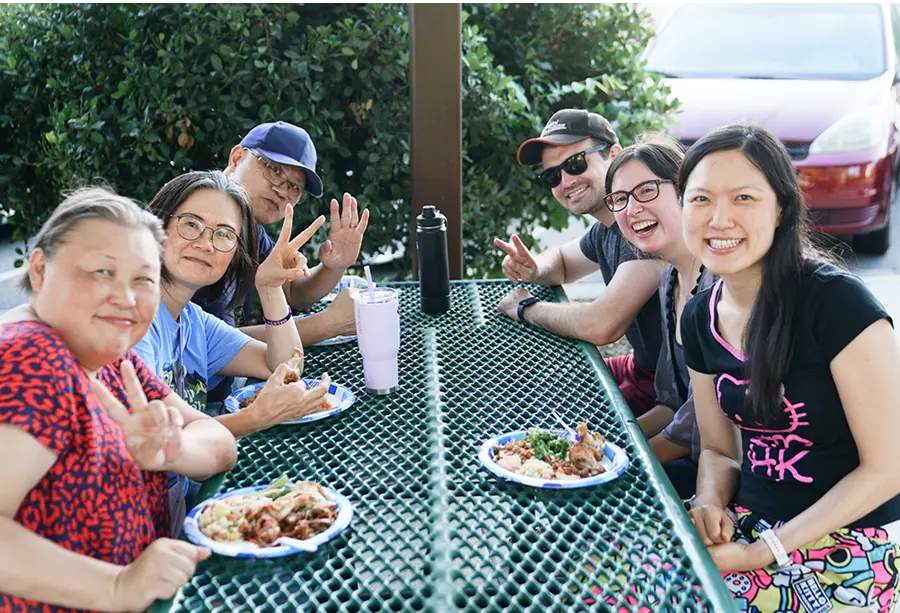 Expressions Church members sharing a meal together at a community lunch, seated around tables outdoors with food and conversation.